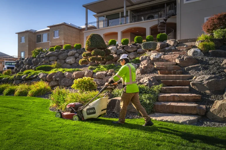 Jesse's Lawn Maintenance crew member mowing a lawn below terraced boulder landscaping